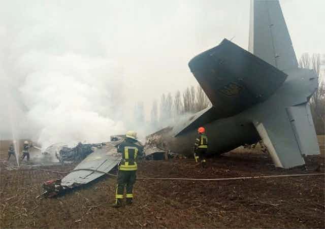 Firefighters attend to the crash site of a military transport aircraft in a field. 