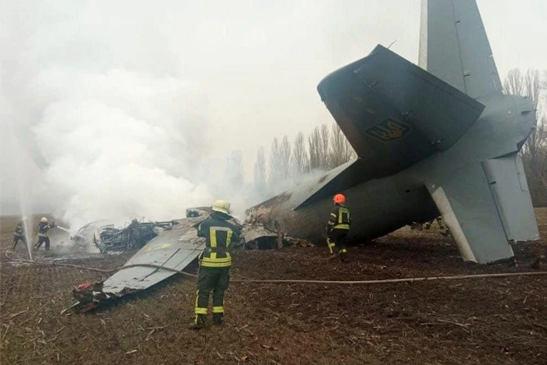Firefighters attend to the crash site of a military transport aircraft in a field.