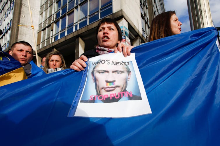 Protestors hold up a photo of Vladimir Putin and a Ukrainian flag.