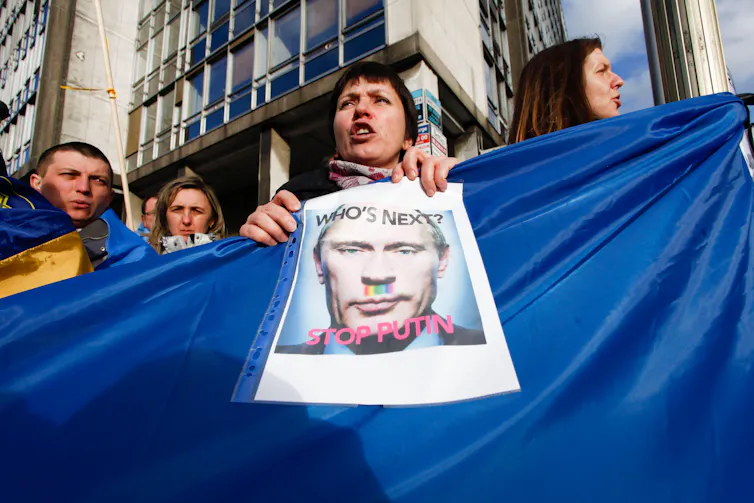 Protestors hold up a photo of Vladimir Putin and a Ukrainian flag.