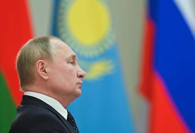 Side profile view of Vladimir Putin with several world flags in the background