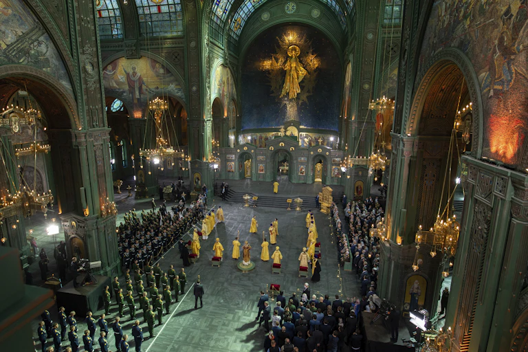 Clergy in yellow robes stand amid worshippers in a cathedral.