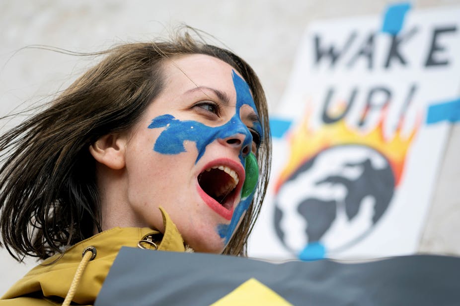 A woman demonstrating with a sign reading: Wake Up! with an image of earth on fire behind her