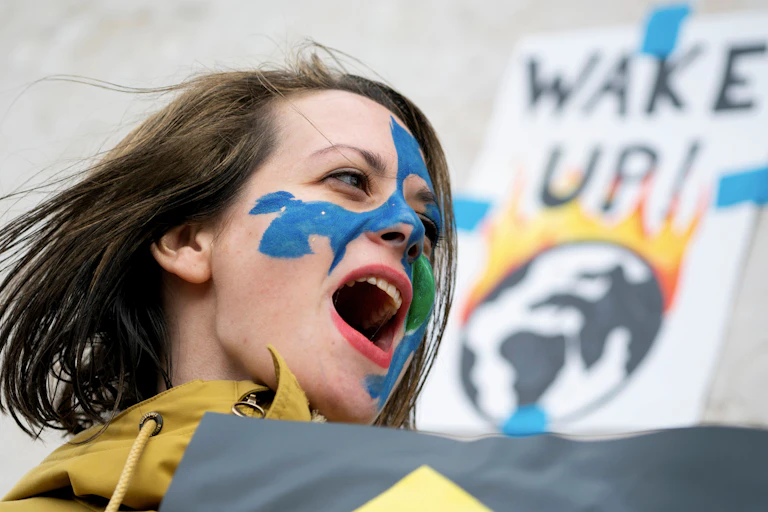 A woman demonstrating with a sign reading: Wake Up! with an image of earth on fire behind her