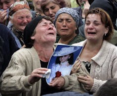 Two women weep as one holds a photo of a child.