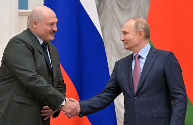 Belarus President Alexander Lukashenko, left, shakes hands with Russian President Vladimir Putin. Behind them stand a Belarus and Russian flag