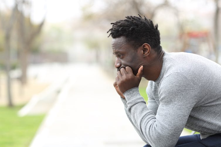 un homme, assis, se tient le menton entre les mains