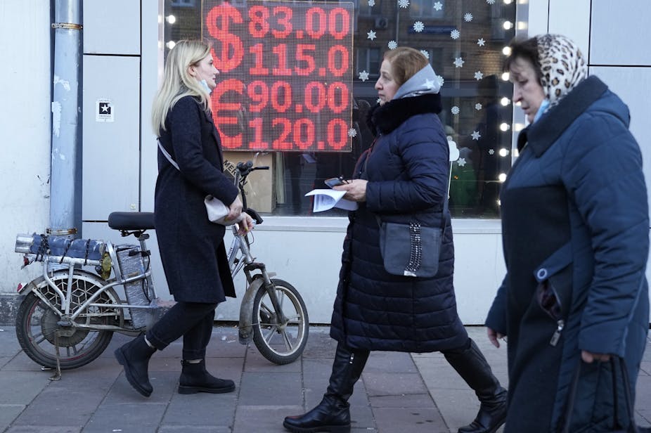 Three women, one holding a bicycle walk past a currency exchange in Moscow, Russia