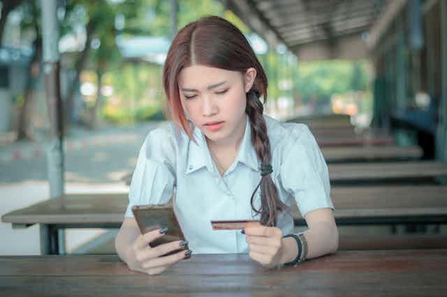 Schoolgirl holding bankcard and looking concerned as she looks at phone