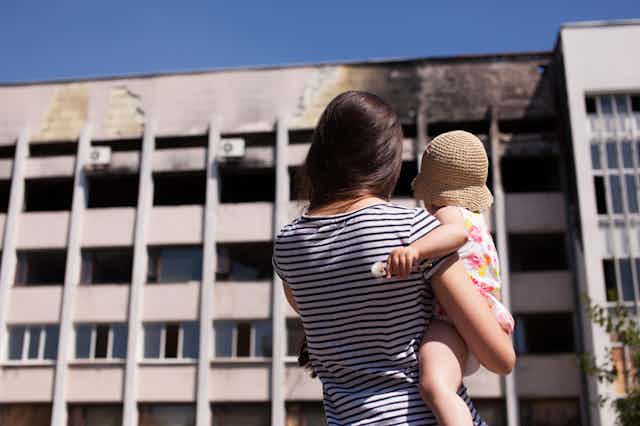 Woman and her baby looking at burned building