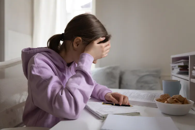 Une ado se tient la tête en tentant de faire ses devoirs