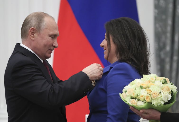 Vladimir Putin pins a medal on to the lapel of RT editor in chief Margarita Simonyan.