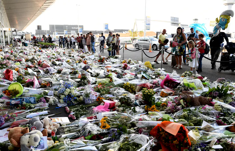 People outside a building looking at large area of ground covered by bouquets of flowers.