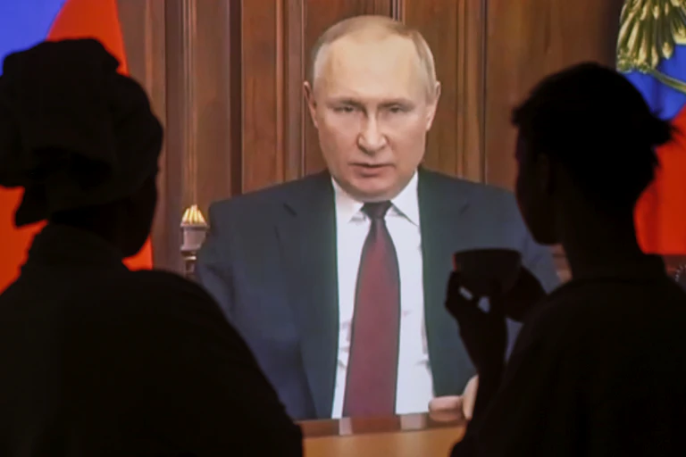 Silhouettes of two people watching Putin on TV screen
