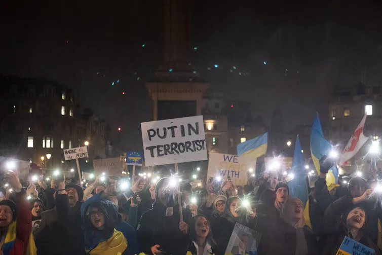 A crowd of protesters in Traflagar Square carrying placards reading 'Putin Terrorist'