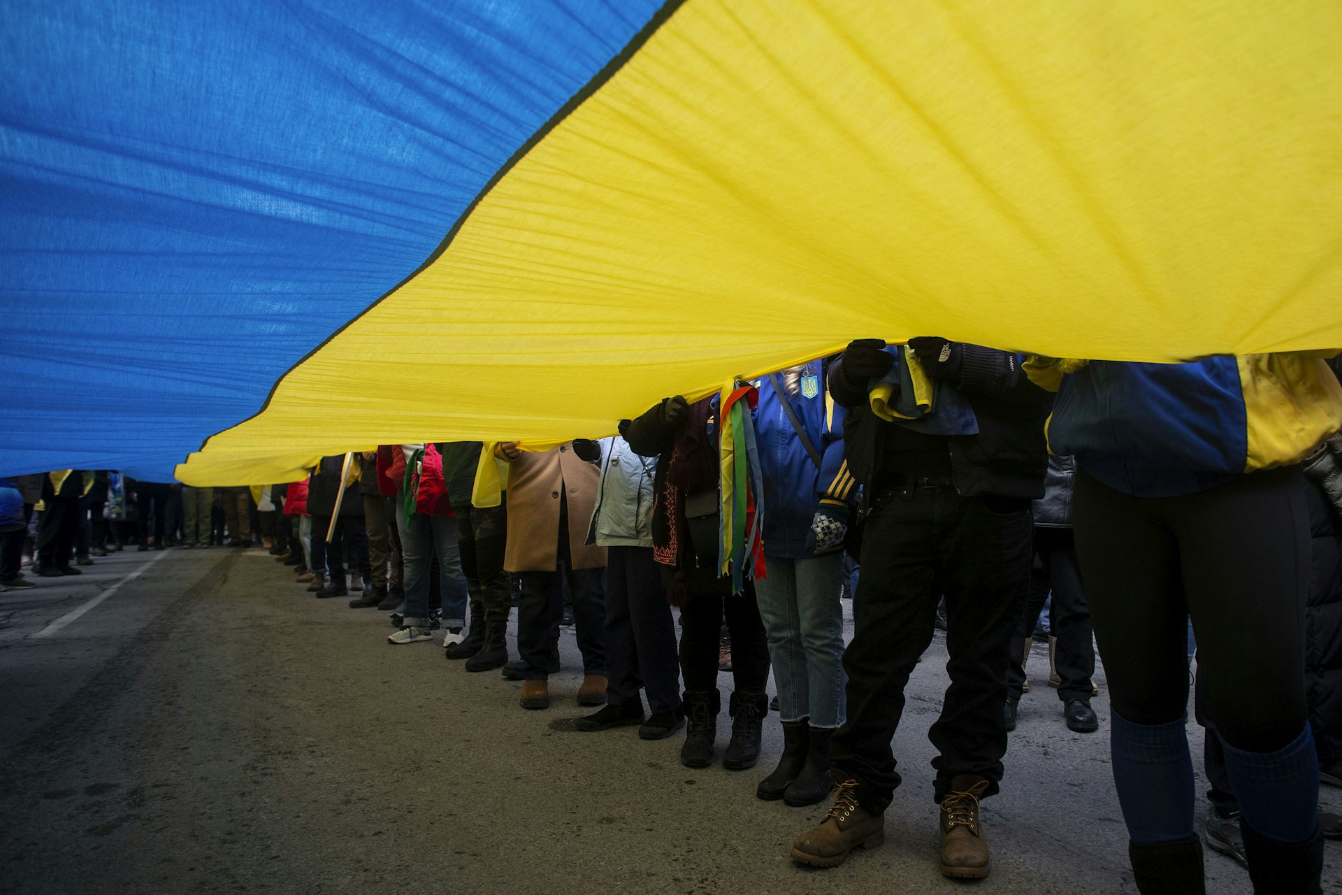 People's legs and feet are seen under a giant Ukrainian flag.