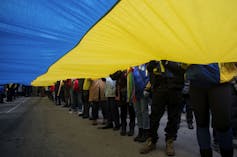 People's legs and feet are seen under a giant Ukrainian flag.