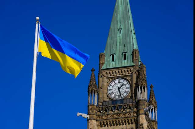 A bright blue and yellow flag flies in a brilliant blue sky with the peace tower behind it.