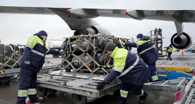 Workers unload military equipment from an airplane.