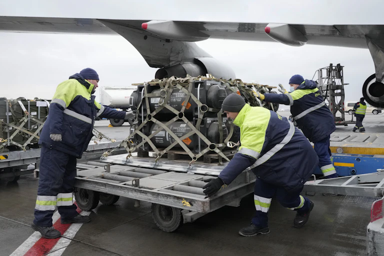 Workers unload military equipment from an airplane.