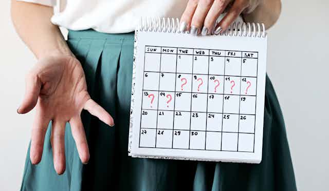 Gros plan sur les mains d'une femme qui tient un calendrier marqué de « ? » pour signaler son retard de règles.