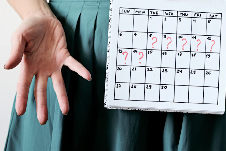 Gros plan sur les mains d'une femme qui tient un calendrier marqué de « ? » pour signaler son retard de règles.