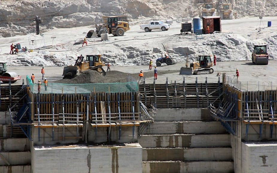 various vehicles are parked on a ridge with workers mixing concrete, creating a vast wall in levels.