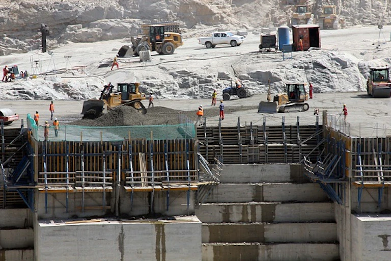 various vehicles are parked on a ridge with workers mixing concrete, creating a vast wall in levels.