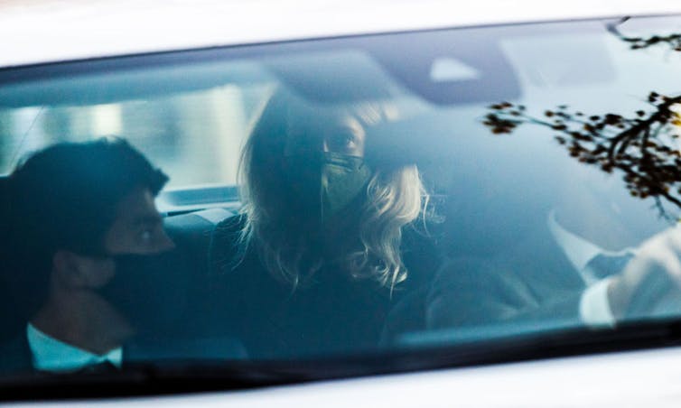 Woman wearing mask seated in back seat of car.