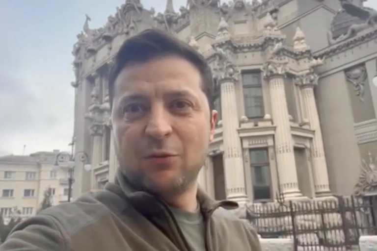 a white man stares ahead in front of a large building with many gargoyles