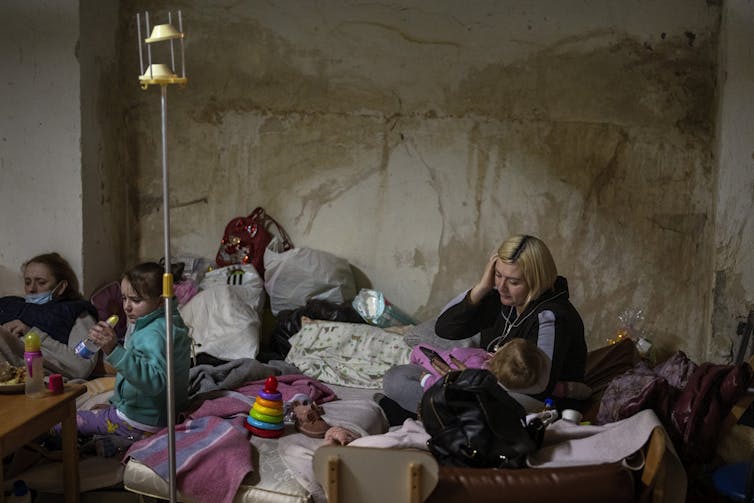 A woman cradles a child as other children site nearby in a basement shelter.