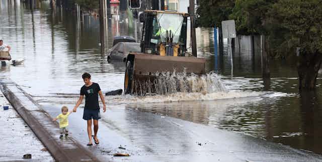 Adult and toddler walk along a street next to floodwater