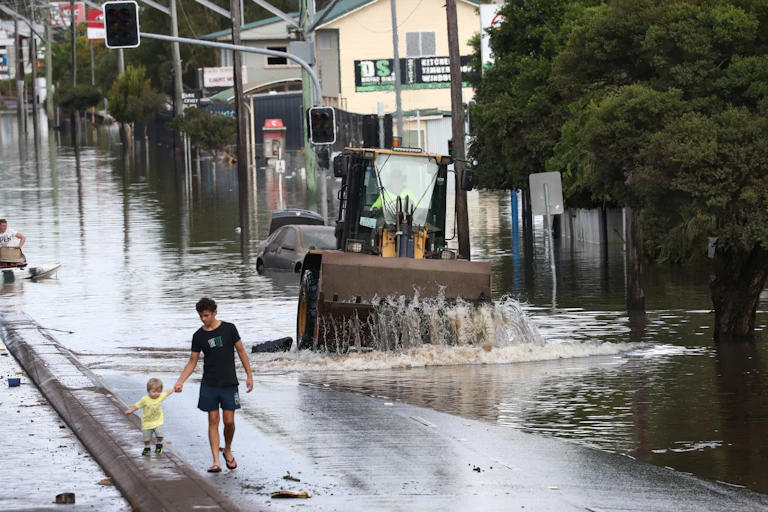 Adult and toddler walk along a street next to floodwater