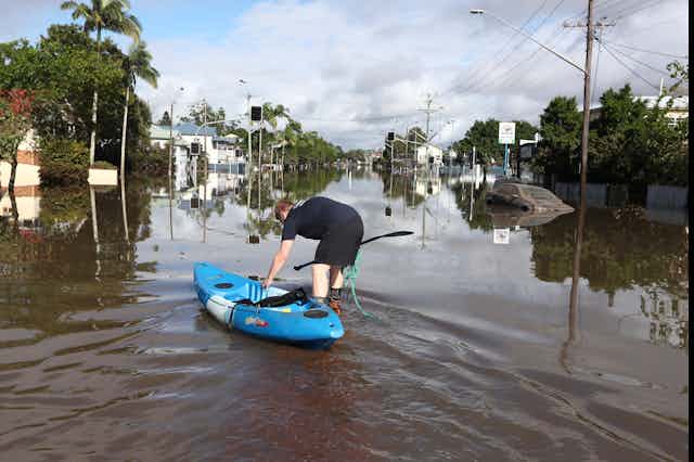 A man guides a blue kayak into a flooded street