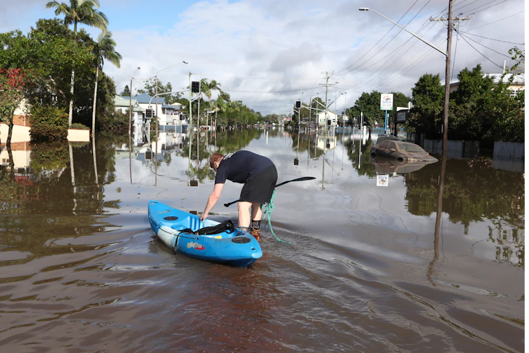 A man guides a blue kayak into a flooded street