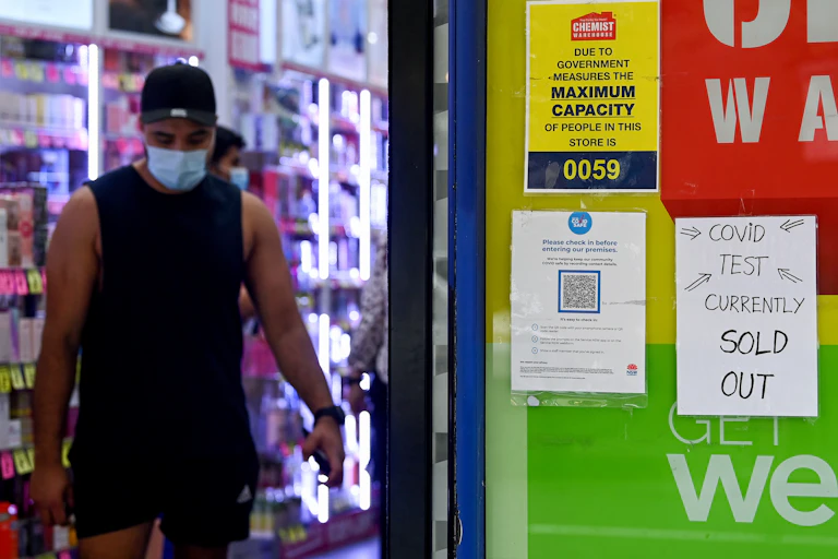A person is walking out of a pharmacy. On the door it says that Covid tests are sold out.