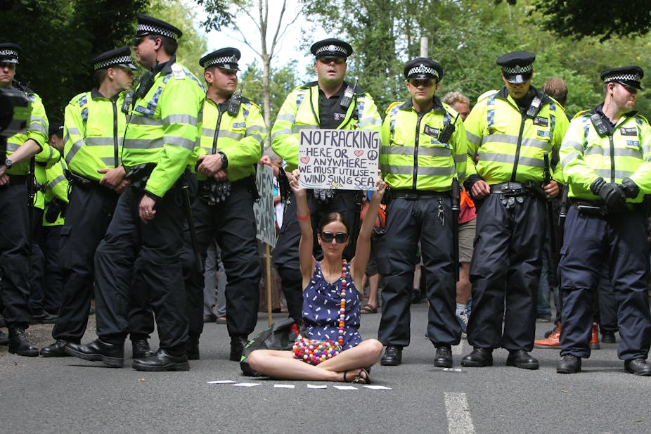 Woman with no fracking placard in front of a line of police