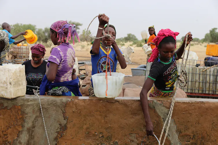 Young people raise plastic containers filled with water from a well.