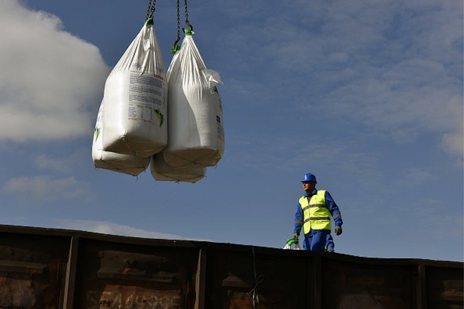 Large bags of fertiliser being loaded onto a platform by a crane as a worker looks on.