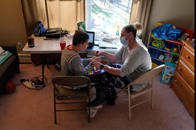 An adult works with a teenager in front of a laptop