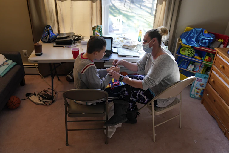 An adult works with a teenager in front of a laptop