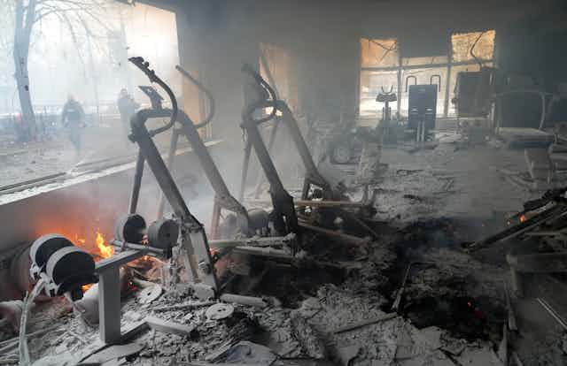 Smoke and flames and ruined treadmills, weight equipment and exercise bikes as people stand on the street outside.