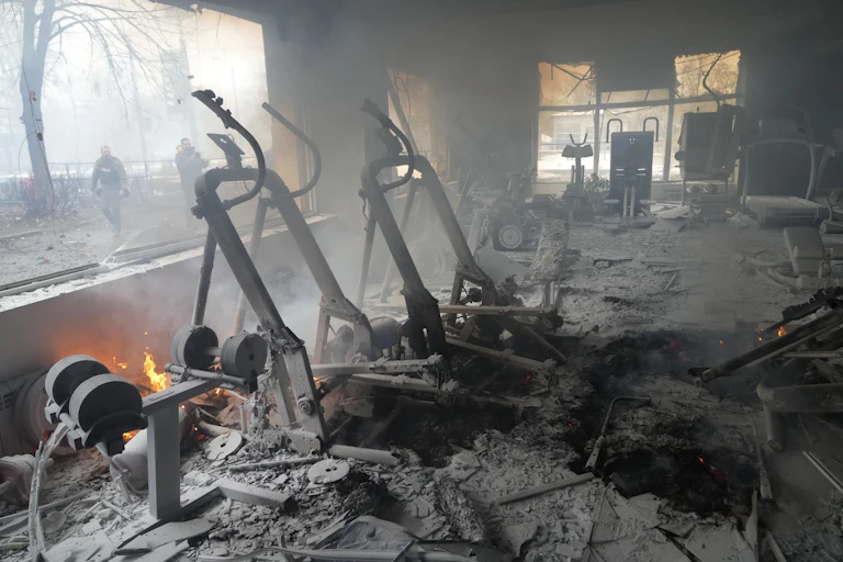 Smoke and flames and ruined treadmills, weight equipment and exercise bikes as people stand on the street outside.