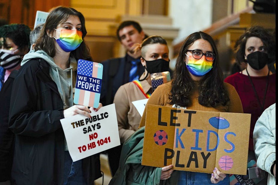 Protesters in rainbow masks and with placards saying "Let Kids Play." 