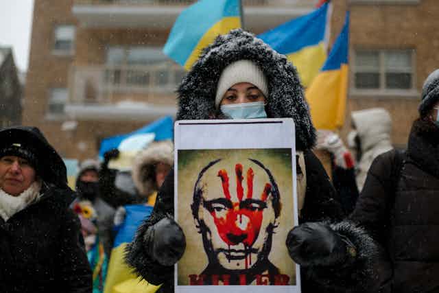 Woman holds a poster of Putin with a large bloody handprint covering his face