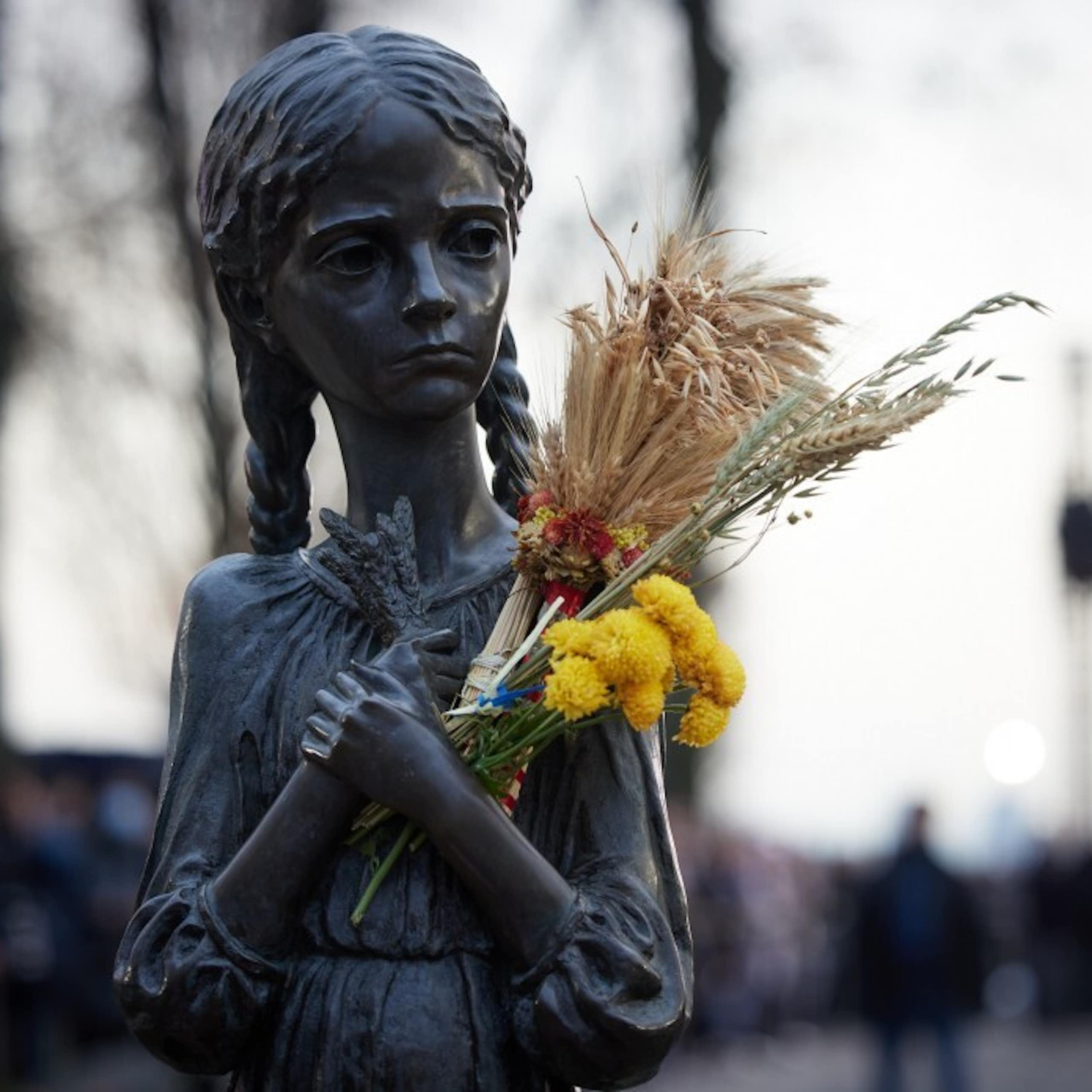 A statue of a girl during the Ukrainian famine, in which someone has placed wheat and flowers.