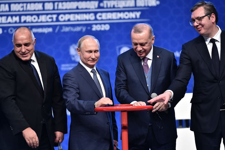 Four men in suits turn a wheel, symbolically opening a pipeline