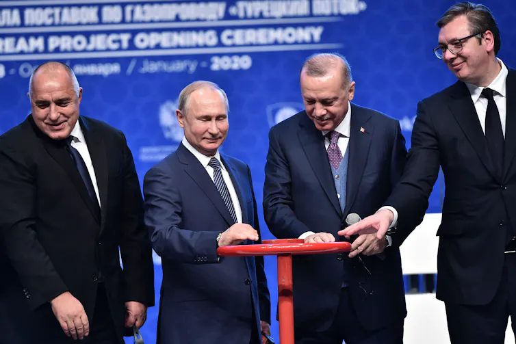 Four men in suits turn a wheel, symbolically opening a pipeline