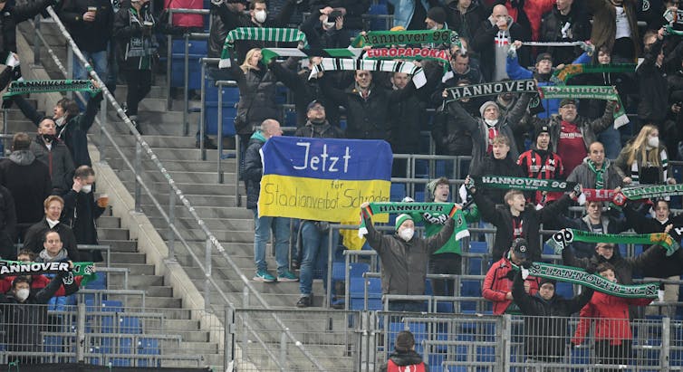 A soccer fan golds up a Ukrainian flag with a banner reading 'Now stadium ban for Schröder'