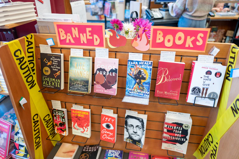 A bookshelf titled "BANNED BOOKS" sits in a library.